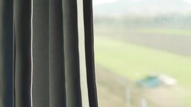 Hareket halindeki trenin penceresinden, sol perdede güneş parlıyor, bulanık evler ve cam pencerenin arkasındaki ülke.