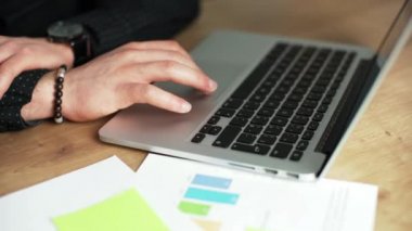 Ofis masasında dizüstü bilgisayarda çalışan genç bir adam. Sırada dokunmatik pedi teslim etmek için bazı belgeler var.