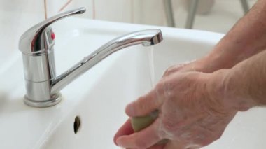 Yaşlı kıdemli bir adam ellerini musluğun altında yıkıyor. Koronavirüs salgını sırasında hijyen konusunda detaylı bilgi veriyor.