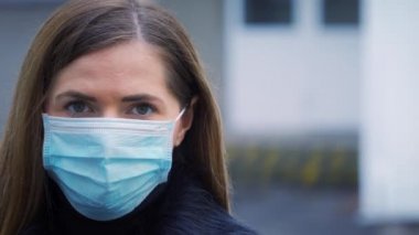 Tek kullanımlık mavi virüs kullanan genç bir kadın ağız maskesi takıyor, yakın plan bir portre. Coronavirus covid-19 salgın önleme kavramı