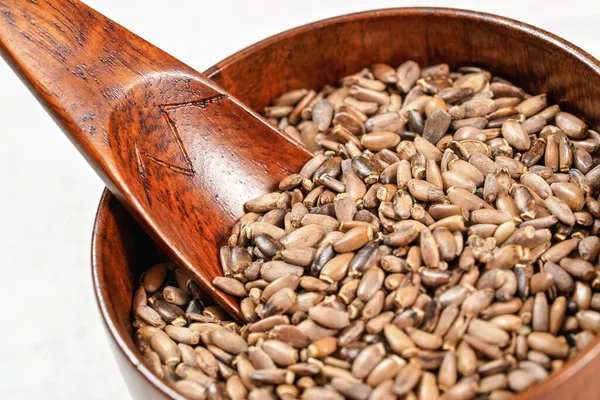 Blessed milk thistle seeds - Silybum marianum - in small wooden cup with scoop on white board, closeup detail — Stock Photo, Image