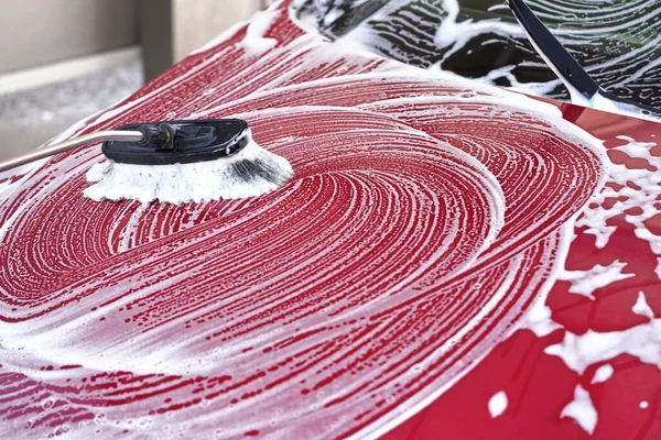 Capucha delantera coche rojo lavado en auto servir carwash, detalle en cepillo dejando golpes en espuma de jabón blanco — Foto de Stock