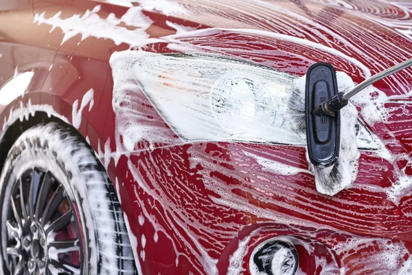 Dettaglio sulla luce anteriore dell'auto rossa lavata in autolavaggio, colpi di sapone bianco sulla superficie — Foto Stock