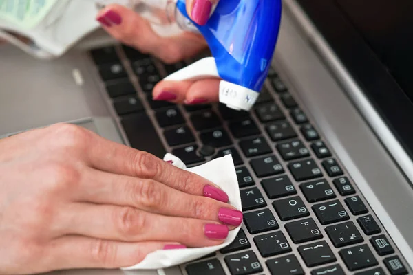 Woman cleaning laptop keyboard with white tissue, detail on her fingers holding paper towel, blue alcohol sprayer near - disinfection concept — Stock Photo, Image