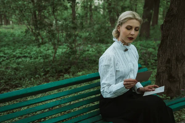 The girl is reading a letter in the park on the bench — Stock Photo, Image