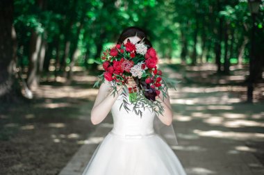 Düğün. Buket. Gelin buketi tutarak. Kırmızı çiçek ve yeşillik. Arka plan orman.