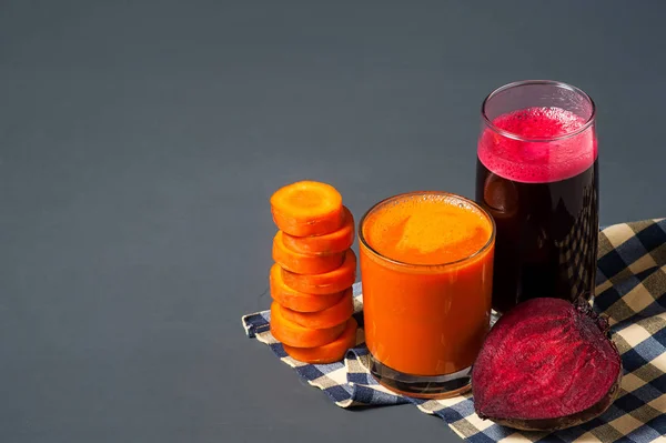 Natural juices from carrots and beets. The juice is poured into a clear glass, next to the chopped carrots and beets. Tasty and healthy juice.