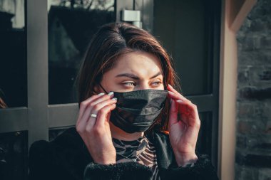 Kız, yüzünde koruyucu steril tıbbi maske takan genç bir kadın Asya sokak gösterilerinde, avuçlarında, ellerinde kameralara bakıyor. Hava kirliliği, virüs, Çin salgını koronavirüs konsepti.