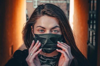 Kız, yüzünde koruyucu steril tıbbi maske takan genç bir kadın Asya sokak gösterilerinde, avuçlarında, ellerinde kameralara bakıyor. Hava kirliliği, virüs, Çin salgını koronavirüs konsepti.