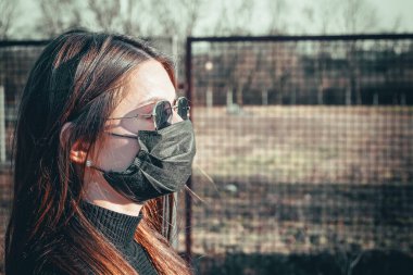 Esmer bir kız sokakta tıbbi bir maskeyle yürüyor, enfeksiyondan korkuyor..