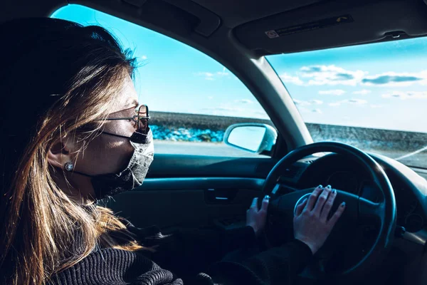 A brunette girl drives a car in a medical mask, fearing infection.
