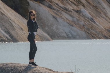 Gölün kıyısında siyah pantolon ve deri ceket giymiş güzel bir genç kız.