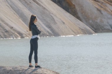 Gölün kıyısında siyah pantolon ve deri ceket giymiş güzel bir genç kız.