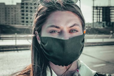Yüz maskesi takan, kameraya bakan genç bir kadının portresi. Grip salgını, toz alerjisi, virüse karşı koruma. Şehir hava kirliliği kavramı