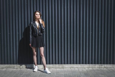 Siyah arka planda parlak makyajlı bir güzellik var. O, siyah bir ceket ve kısa bir etek giydi, külotlu çorabı üzerinde bir ağ ve beyaz spor ayakkabıları vardı..