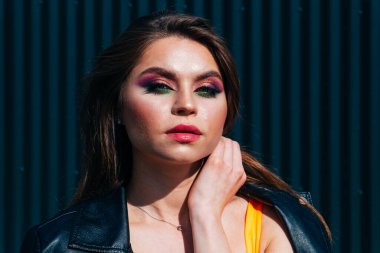 Siyah arka planda parlak makyajlı bir güzellik var. O, siyah bir ceket ve kısa bir etek giydi, külotlu çorabı üzerinde bir ağ ve beyaz spor ayakkabıları vardı..