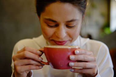 Bir kafede kapuçino içen güzel genç bir kız kalp şeklinde kahve çiziyor, pembe kupa, kahve içiyor ve eğleniyor.