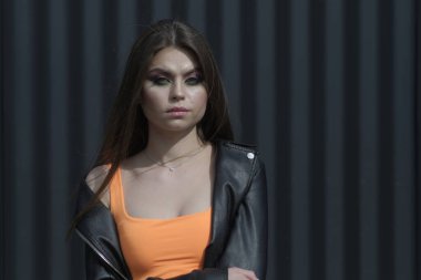 Parlak turuncu bir bluz ve siyah deri ceket giymiş güzel esmer bir kızın portresi doğrudan kameraya bakıyor.