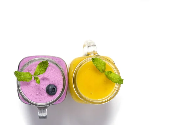 Purple and yellow smoothies with mint in mason jar glass with berries and mint. Above view on white table. Healthy food.