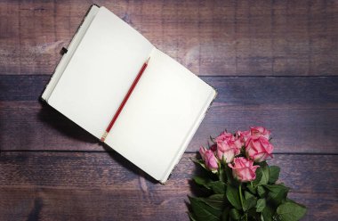 Rustik kahverengi ahşap masa üzerinde üstten görünüm defter ve kırmızı ve pembe güller çiçek boş levha. Uzay kopyalayın. Düz yatıyordu, en iyi görünümü office tablo Resepsiyon. Güllü, kadınsı Resepsiyon çalışma günlüğü. 