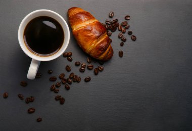 Taze kruvasan ve kahve ve taş masada kavrulmuş fasulye. Üstten Görünüm kopya alanı ile. Taze kruvasan ve kahve ve taş masada kavrulmuş fasulye. Üstten Görünüm kopya alanı ile. Siyah arka plan üzerine kahve kupa. 