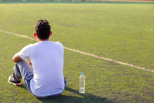 運動後のスポーツスタジアムの芝生の上ののどが渇いた男 男の近くの草の上に純水のボトル — ストック写真