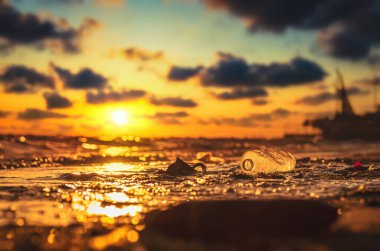 Plajda plastik su şişesi, çevre kirliliği. Kirli sahil ve gün batımı.