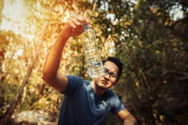Bir adam ormanda ve sıcak havada şişede az su gösterir..