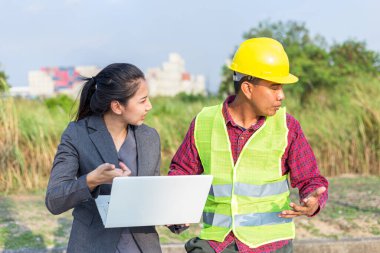 Sert şapkalı ve üniformalı, genç bir kadınla birlikte erkekler. Mimarlar, mühendislerden oluşan ekip çalışmaları tartışıyor. Bir kadın dizüstü bilgisayar tutun.
