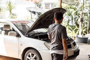  Bir adam kırık arabayı ve açık kaputu kontrol ediyor. Araba bozuldu ve kaza yaptı..