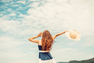 Yaz tatilinde şapkalı ve elbiseli mutlu kadın adanın kumsalının tadını çıkarıyor..