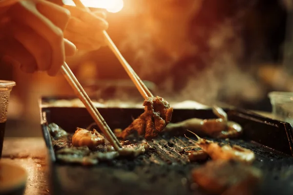 People cooking meat and grill. People use chopsticks.