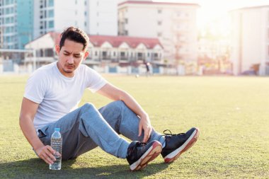Egzersiz den sonra spor stadyumunda çim üzerinde susamış adam. Bir adamın yanında çimenlerin üzerinde bir şişe saf su.
