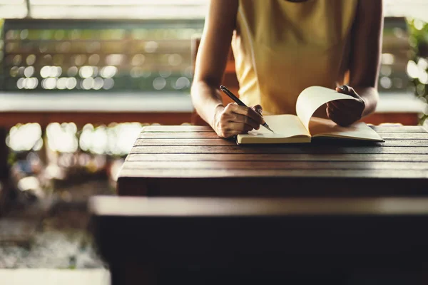 Hand hold pen and writing a book on the table.