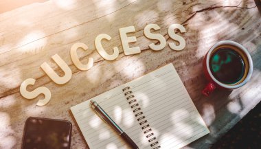 Kağıt notun, kahvenin, kalemin ve cep telefonunun yanındaki tahta masada 