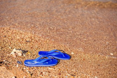 Sahilde bir çift parmak arası terlik ve su akışı.