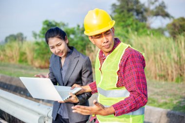 Sert şapkalı ve üniformalı, genç bir kadınla birlikte erkekler. Mimarlar, mühendislerden oluşan ekip çalışmaları tartışıyor. Bir kadın dizüstü bilgisayar tutun.