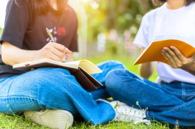Üniversite öğrencileri çimlerin üzerinde oturup kitap okuyorlar..