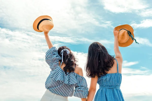 Two happy girl hold hat and raise arms in the sky. People traveling relaxing and enjoying  at summer