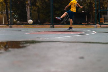 Bir çocuk parkta futsal pratiği yapıyor..