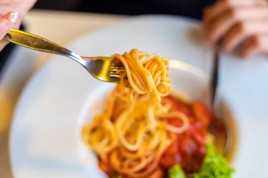 Çatallı spagetti. Kız spagettiyle çatal kullanıyor. Kırmızı soslu makarna..