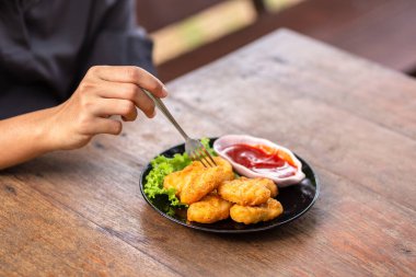 Tavuk Nuggets bir çatal ve Dip sos üzerine kazıklı. Bir kadın Nuggets yemek.