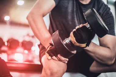 Spor salonunda dambılı kaldıran genç bir adam.