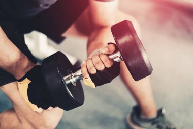Spor salonunda dambılı kaldıran genç bir adam.