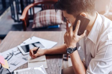 İş adamı konuşmak için cep telefonu kullanır ve kağıt grafikte verileri kontrol etmek için sağ el kalem kullanır..