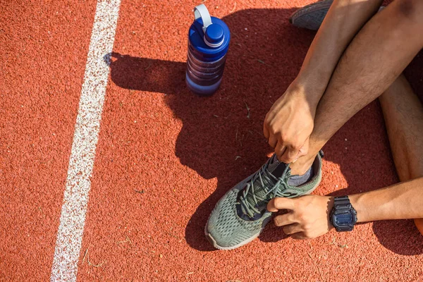 attractive brunette man tie their shoes before run on  track race. A man at sport stadium. water bottle on the ground near sport man.