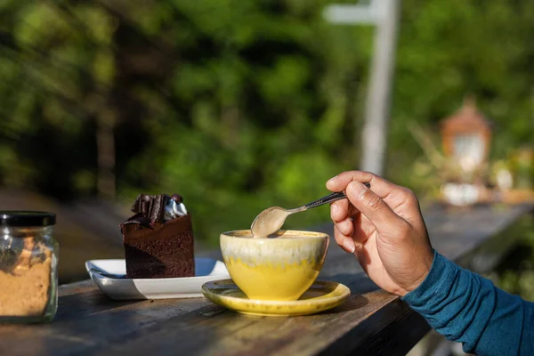 man hand use spoon mix coffee and sugar in the morning. cake and coffee on the wood table.