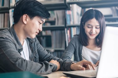 Kütüphanede birlikte okuyup okuyan lise ya da üniversite öğrencileri. Öğrenci kütüphanede dizüstü bilgisayar kullanır.