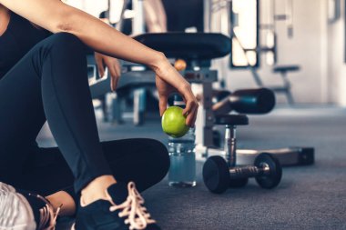 Spor salonunda kadın egzersizi ve dinlenme. Elma meyvesi tutan eller spor yaparken yanında dambıl ve su şişesi vardı..