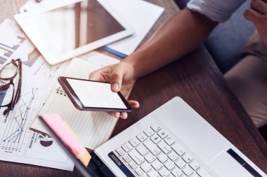 İş adamı çalışmak ve mesajları kontrol etmek için cep telefonunu kullanır. Laptop, döküman çizelgesi masada..